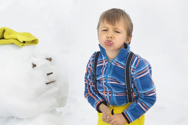 Маленький сердитый мальчик и снеговик — стоковое фото