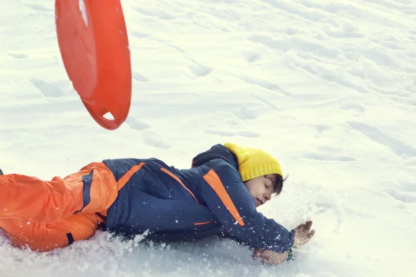 Mały chłopiec sankach bardzo szybko i spada na śniegu — Zdjęcie stockowe