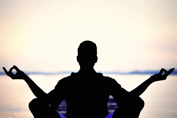 Contraluz del hombre haciendo yoga frente al mar —  Fotos de Stock