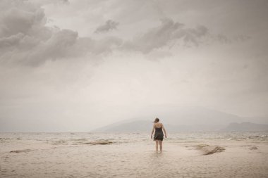 Rüzgarda savrulan bir kadın denizin ötesindeki sonsuzluğa doğru yürüyor.