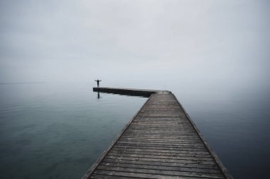 Kollarını ışığa doğru kaldırmış bir adam. Akşam ışığında denizde bir rıhtımın ucunda.