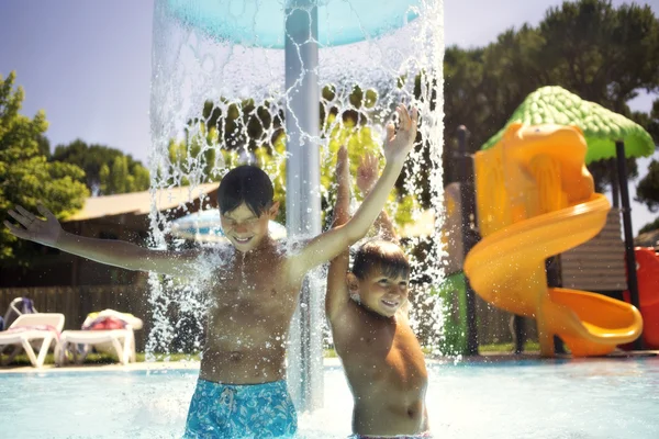 Glada pojkar leker med fontänen vatten i poolen — Stockfoto
