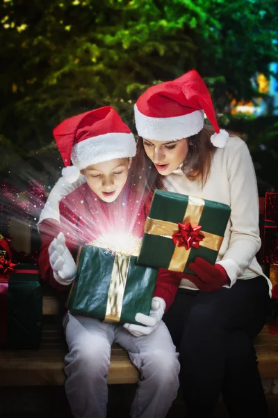 Mãe dá a seu filho uma caixa de presente de Natal com raios de luz e — Fotografia de Stock