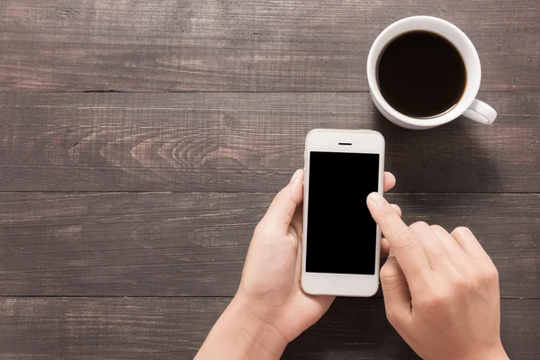 Использование смартфона рядом с кофе на деревянном столе — стоковое фото