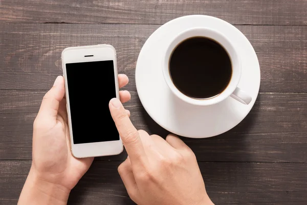 Использование смартфона рядом с кофе на деревянном столе — стоковое фото