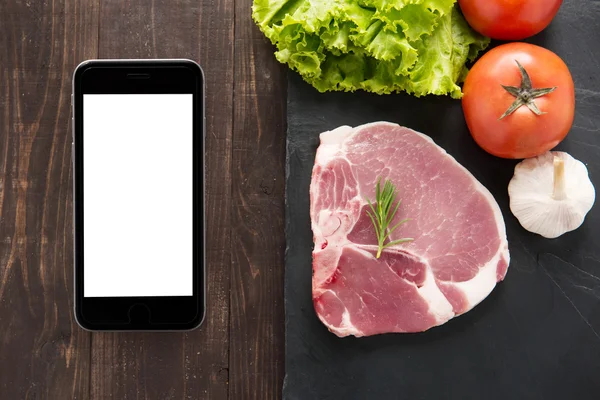 Вид сверху сырой свинины и овощей на доске со смартфоном — стоковое фото