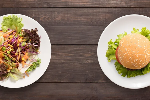 Čerstvý salát a burger na dřevěné pozadí. kontrastní potravin — Stock fotografie