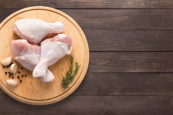 Baquetas de frango cru na placa de corte em fundo de madeira . — Fotografia de Stock