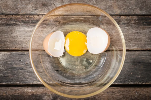 Popraskané slepičí vejce s žloutku a egg shell na misky, dřevěné zpět — Stock fotografie
