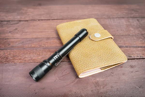 Leather bag an fashioned flashlight, on wooden background — Stock Photo, Image