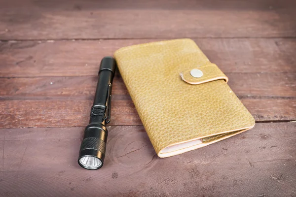 Leather bag an fashioned flashlight, on wooden background — Stock Photo, Image