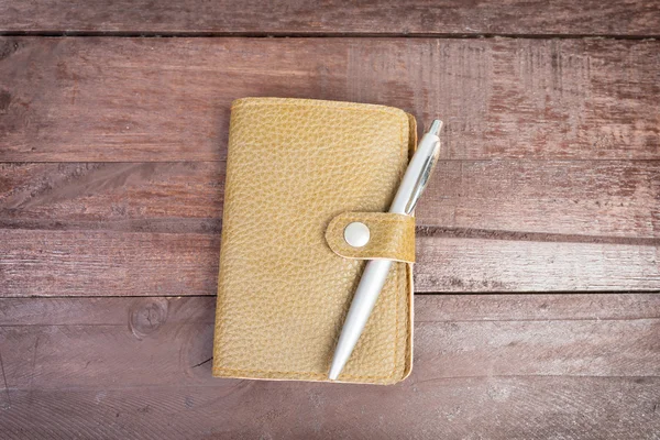 Pen on top of yellow organizer with leather cover on wooden back — Stock Photo, Image