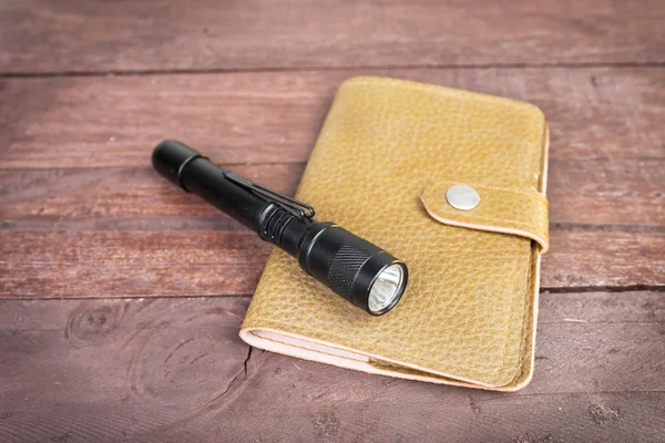 Leather bag an fashioned flashlight, on wooden background — Stock Photo, Image