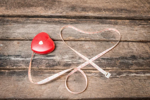 A measuring tape shaping a heart on wooden background Stock Image