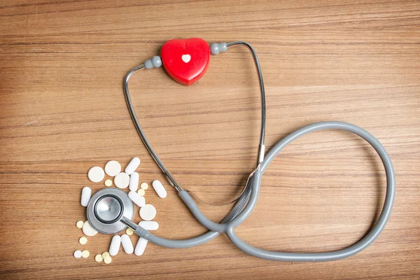 Heart with pills and stethoscope on wooden background — Stock Photo, Image