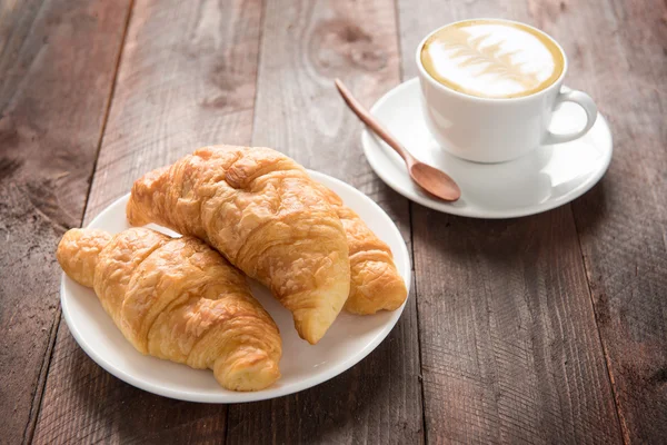 Čerstvě upečené croissanty a kávu na dřevěný stůl — Stock fotografie