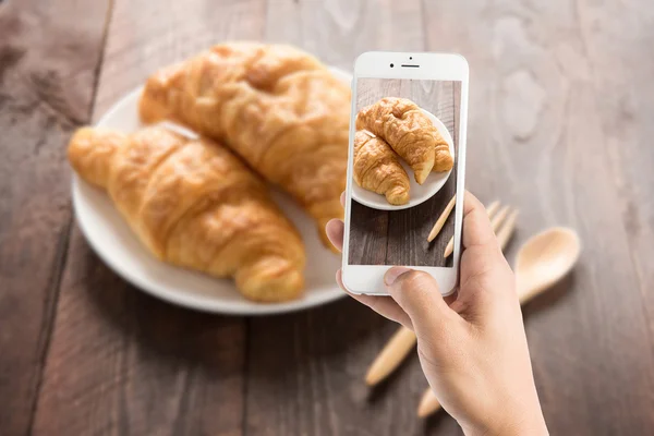 Het nemen van foto van vers gebakken croissants op houten tafel — Stockfoto