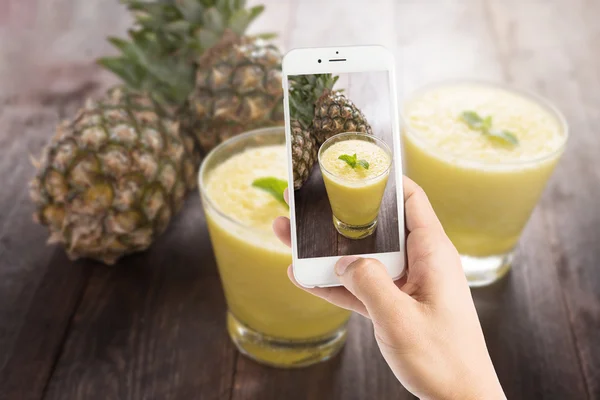 Taking photo of pineapple smoothie on wooden table — Stock Photo, Image