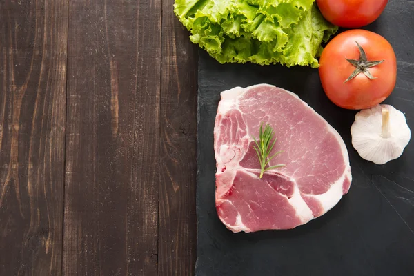 Carne di maiale cruda vista dall'alto su lavagna e verdure su backgro in legno — Foto Stock