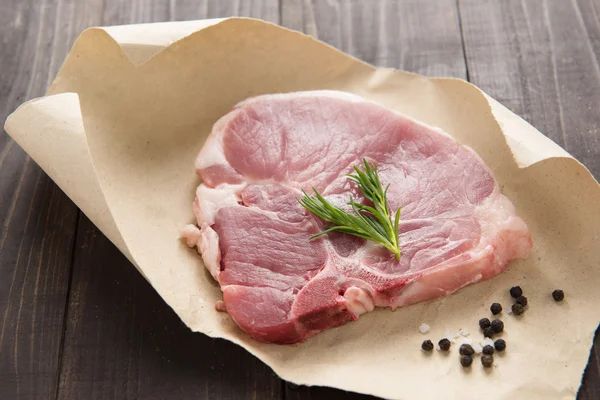 Raw pork chop steak on paper and wooden background — Stock Photo, Image