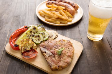 Izgara biftek salata ve bira ve kızarmış patates sosis ahşap bakcground üzerinde.