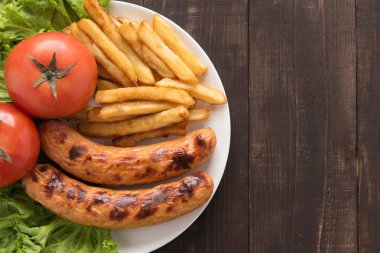 Grilled sausage and vegetables with french fries on wooden background clipart