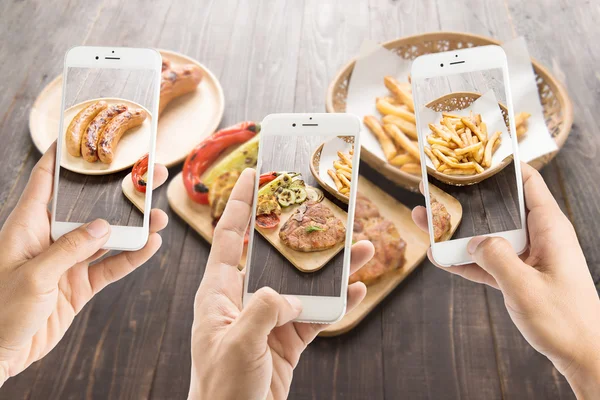 Sosis ve domuz pirzolası ve patates kızartması fotoğraf çekmek için akıllı telefonlar kullanan arkadaşlar