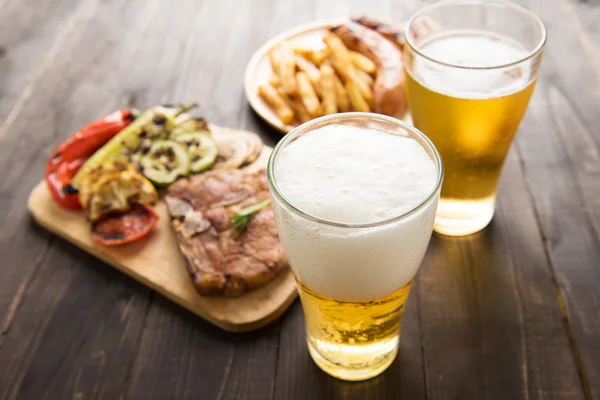 Пиво в склянці з гастрономічним стейком та картоплею фрі на дерев'яному фоні — стокове фото