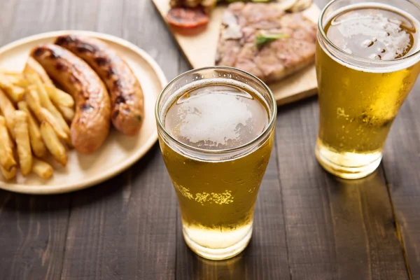 Пиво в склянці з гастрономічним стейком та картоплею фрі на дерев'яному фоні — стокове фото