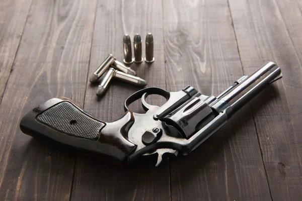 Pistola de revólver preto com balas isoladas em fundo de madeira — Fotografia de Stock