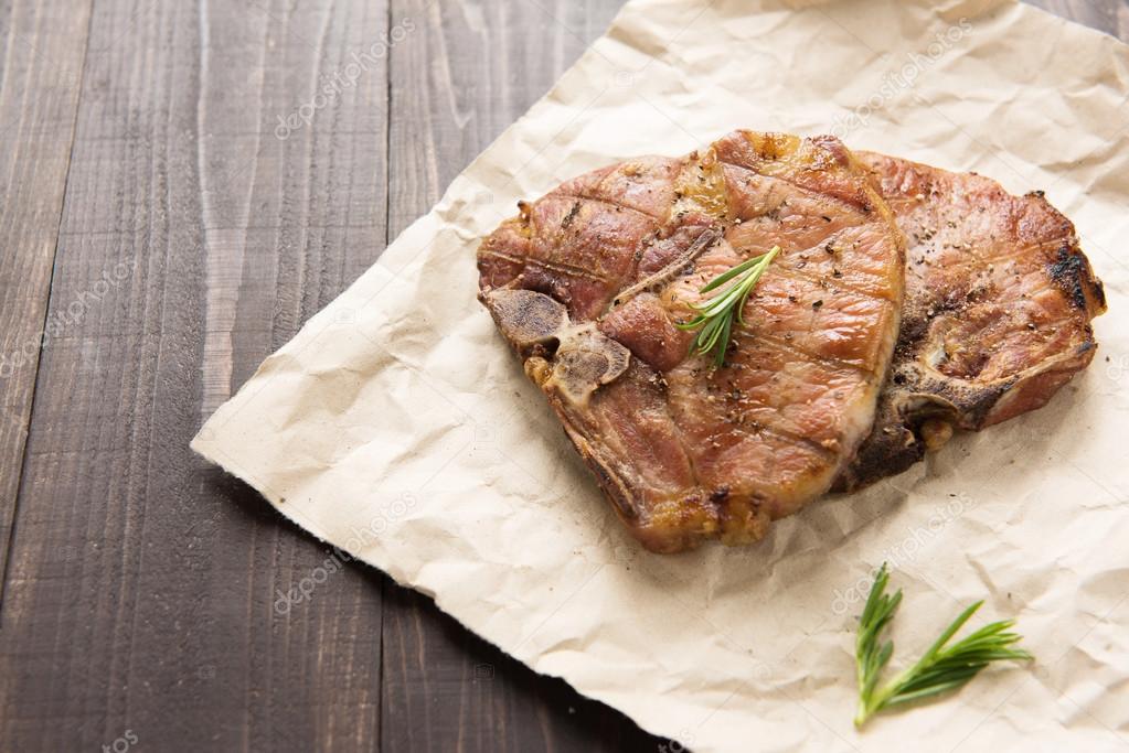 Grilled pork with herbs on a paper on wooden background