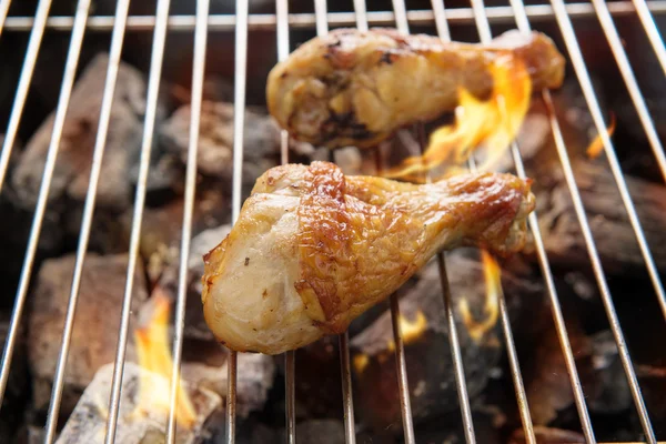 Pernas de frango grelhando sobre chamas em um churrasco . — Fotografia de Stock