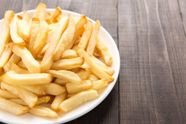Ahşap arka planda beyaz tabakta patates kızartması.