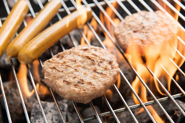 Hamburgers en worstjes koken over vlammen op grill. — Stockfoto