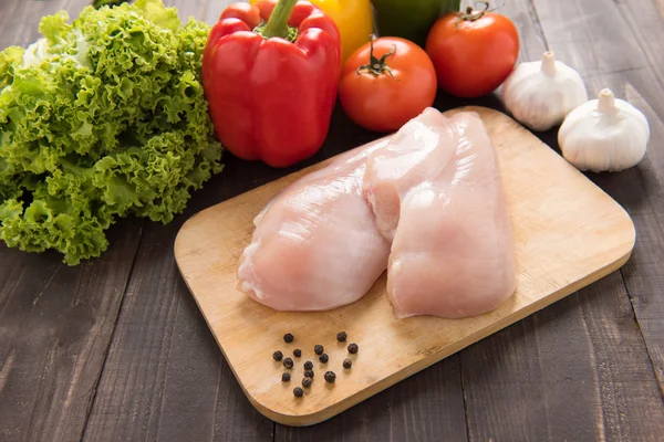 Filetes de peito de frango cru e vegetais em fundo de madeira . — Fotografia de Stock