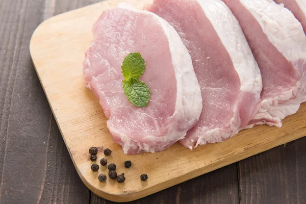 Ruwe varkensvlees op snijplank op houten achtergrond. — Stockfoto