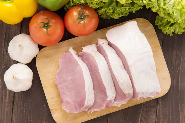 Raw pork on cutting board and vegetables. — Stock Photo, Image