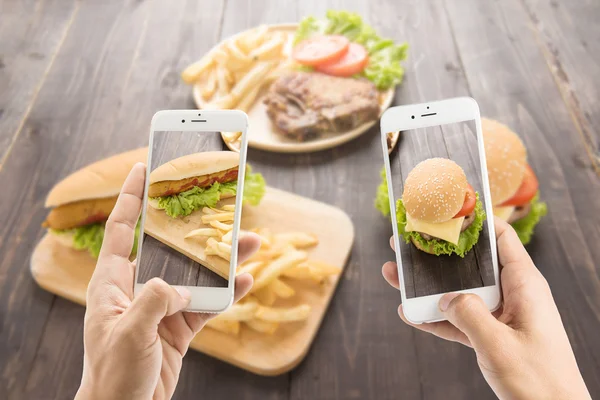 Amigos usando teléfonos inteligentes para tomar fotos de hot dog y hamburguesa — Foto de Stock