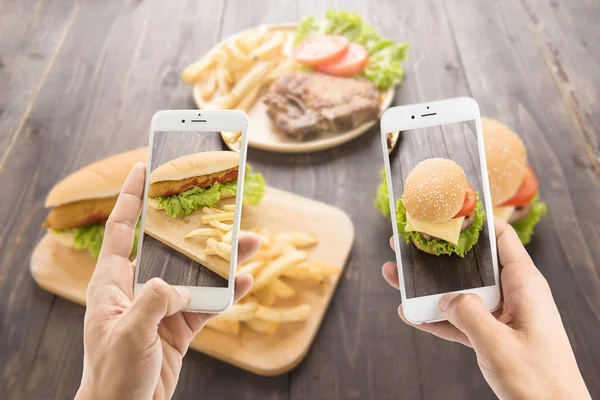 Amigos usando smartphones para tirar fotos de cachorro-quente e hamburgo — Fotografia de Stock