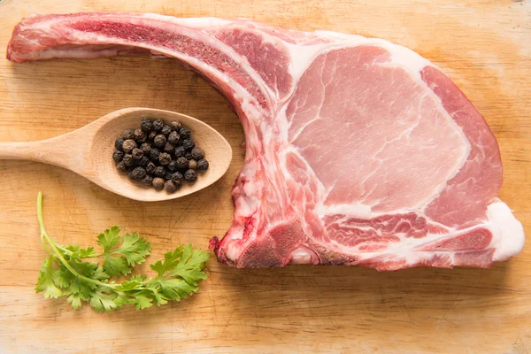 Frische rohe Schweinekoteletts und Pfeffer in einem Löffel auf Holzgrund. — Stockfoto