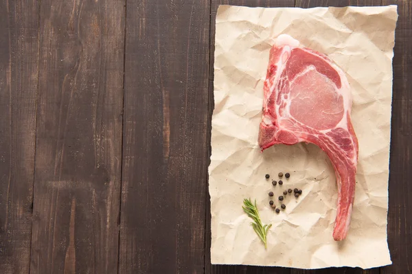 Bistecca di costoletta di maiale cruda vista dall'alto su carta su sfondo di legno — Foto Stock