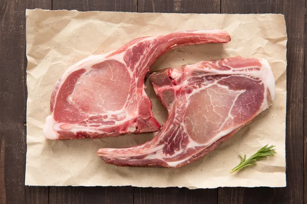 Bistecca di costoletta di maiale cruda vista dall'alto su carta su sfondo di legno — Foto Stock