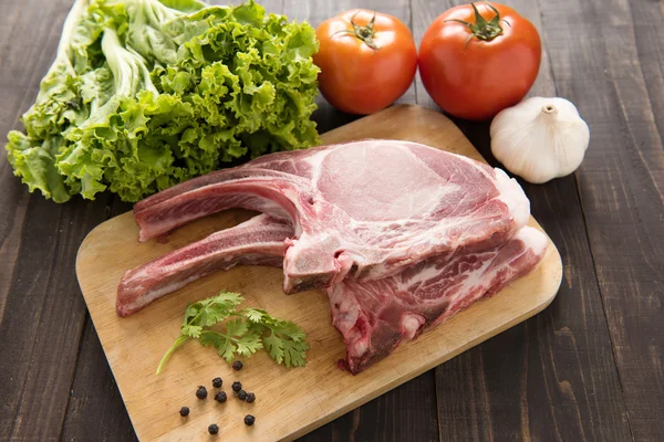 Свежая сырая свиная отбивная и овощи на деревянном фоне . — стоковое фото