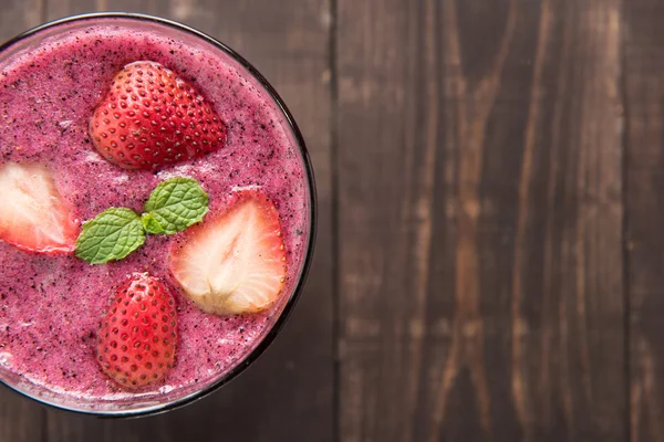 Strawberry smoothie in glass on wooden background, with a lot of — Stock Photo, Image