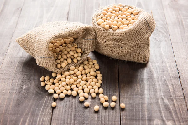 Soybean in a bag on wooden background. — Stock Photo, Image
