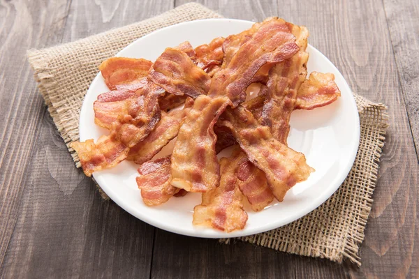 Closeup of fried bacon strips on white plate — Stock Photo, Image