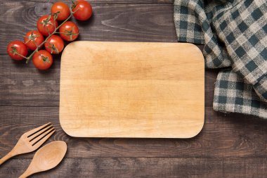 Cutting board with tomato, fork and spoon on wooden background clipart