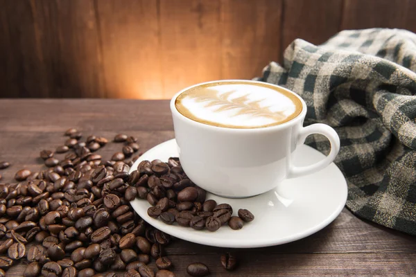 ถ้วยกาแฟและถั่วกาแฟบนพื้นหลังไม้ — ภาพถ่ายสต็อก