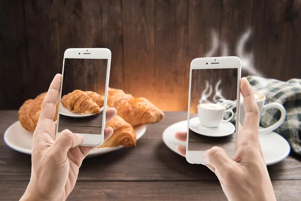 Mengambil foto cangkir kopi dan croissant di latar belakang kayu — Stok Foto