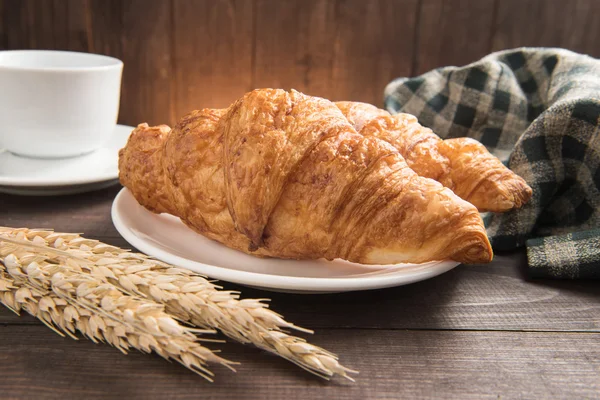 Ontbijt croissant en koffie cup op houten achtergrond — Stockfoto